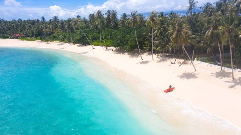 Pemain papan dayung dengan papan merah di pantai biru toska
